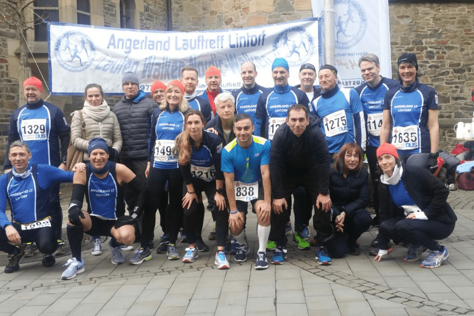 Gruppe von L&auml;ufern in blauen T-Shirts posiert vor einem Banner beim Angeland Lauftreff.