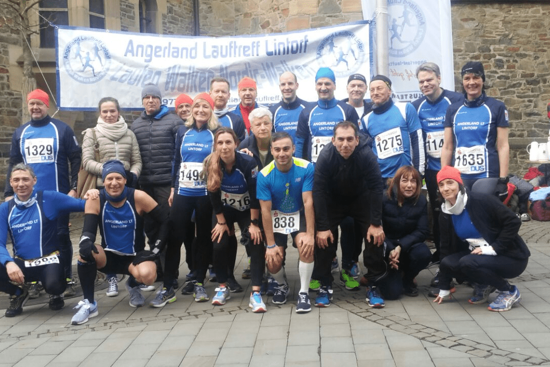 Gruppe von Läufern in blauen T-Shirts posiert vor einem Banner beim Angeland Lauftreff.