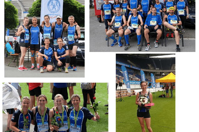 Gruppenfoto von L&auml;ufern in blauen Trikots, um einen Meeting Point Banner, vor einem Stadion.