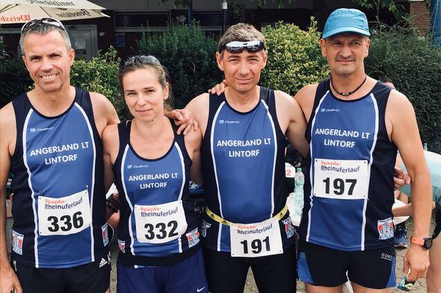 Vier L&auml;ufer in Sportbekleidung stehen l&auml;chelnd zusammen, auf einem Wettkampf im Freien.