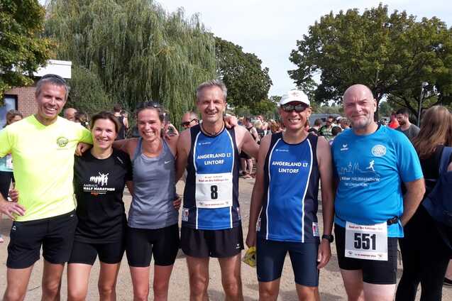 Gruppe von sechs L&auml;ufern in Sportkleidung, posierend vor einer Menschenmenge beim Wettkampf.