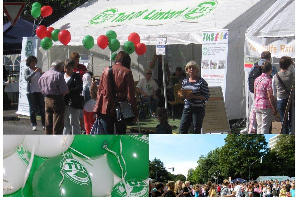 Menschen stehen vor einem Festzelt mit gr&uuml;nen und roten Ballons, w&auml;hrend eine Gruppe im Hintergrund tanzt.
