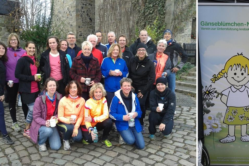 Gruppe von Personen mit Getr&auml;nken, posierend vor einer Mauer, neben einem Plakat des Vereins G&auml;nsebl&uuml;mchen-NRW e.V.