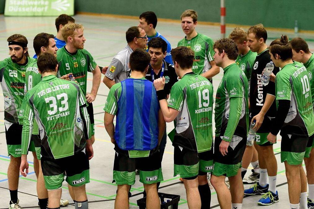 Gruppe von Handballspielern in grünen Trikots hört einem Trainer während einer Besprechung zu.
