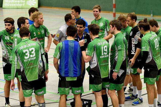 Gruppe von Handballspielern in gr&uuml;nen Trikots h&ouml;rt einem Trainer w&auml;hrend einer Besprechung zu.