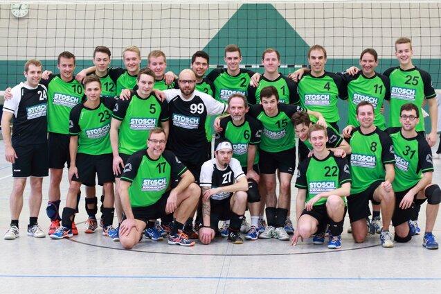 Gruppenfoto einer m&auml;nnlichen Volleyballmannschaft in gr&uuml;nen Trikots, posierend vor einem Volleyballnetz in einer Halle.