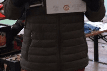 Junger Mann mit Mütze hält eine Urkunde und einen Pokal in einer festlichen Umgebung.