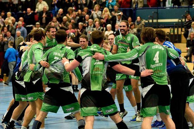 Feiernde Handballmannschaft in gr&uuml;nen Trikots umarmt sich in einer sportlichen Halle vor jubelndem Publikum.