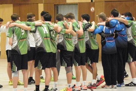 Gruppe von Handballspielern in gr&uuml;nen Trikots, die sich im Kreis umarmen und sich auf ein Spiel vorbereiten.