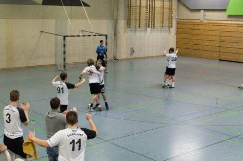 Spieler feiern einen Torerfolg in einer Halle, w&auml;hrend Teamkollegen auf der Bank jubeln. Handballspiel in Aktion.