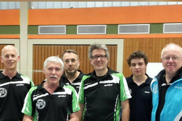 Sechs M&auml;nner in Tischtennis-Trainingsanz&uuml;gen posieren l&auml;chelnd in einer Sporthalle.