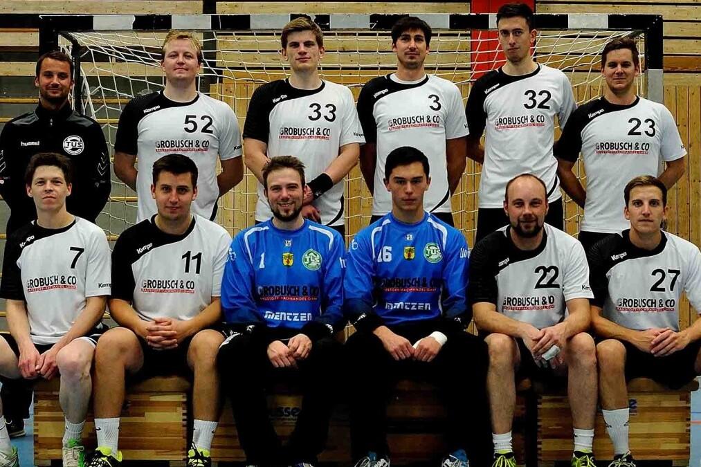 Mannschaftsfoto einer Handballmannschaft mit Spielern in Trikots, auf einer Sporthalle vor dem Tor.