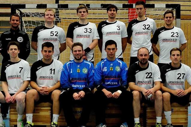 Mannschaftsfoto einer Handballmannschaft mit Spielern in Trikots, auf einer Sporthalle vor dem Tor.