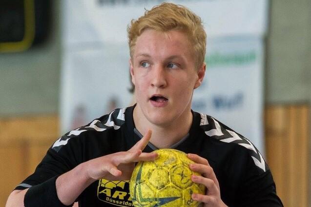 Handballspieler in schwarzem Trikot mit gelbem Ball in der Hand, bereit zu passen oder zu werfen. Hintergrund unscharf.