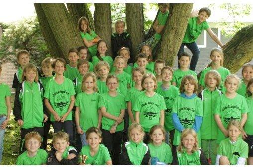 Gruppe von Kindern in grünen T-Shirts posiert unter einem Baum, einige sitzen, andere stehen und einige klettern.