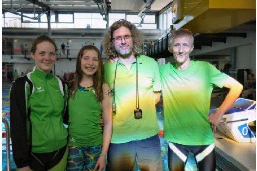 Gruppenfoto von Schwimmern in gr&uuml;nen Shirts am Pool, begleitet von Trainern. Unten ein Schwimmer im Wasser mit Badekappe.