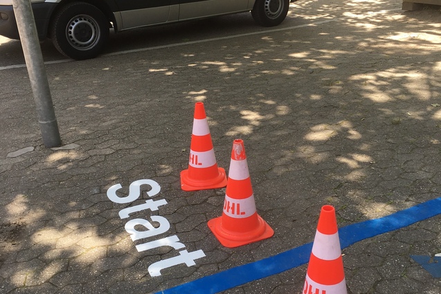 Startlinie mit wei&szlig;en Buchstaben und aufgestellten orangen Verkehrsh&uuml;tchen auf dem Boden einer Asphaltfl&auml;che.
