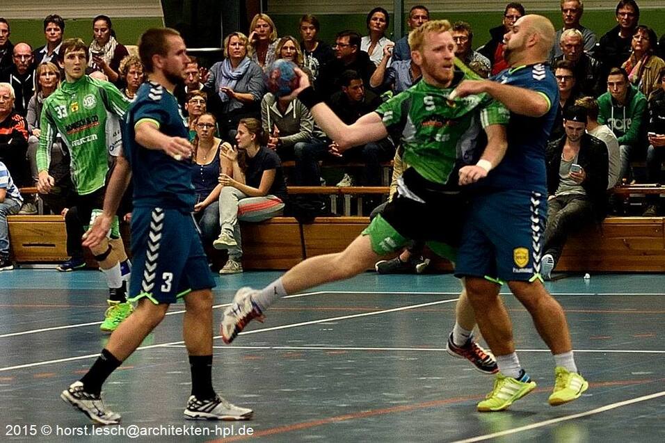 Zwei Handballspieler k&auml;mpfen um den Ball in einem lebhaften Spiel vor einer Zuschauermenge.
