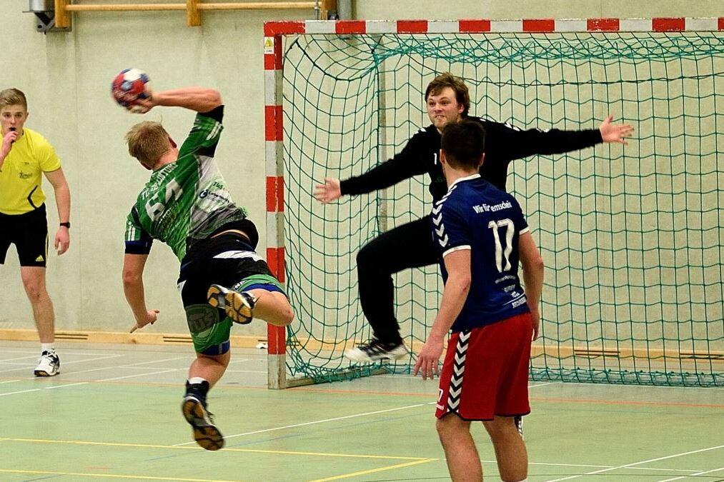 Handballspieler springt zum Wurf auf das Tor, während ein Torwart sich zur Abwehr bereit macht und Schiedsrichter zuschaut.