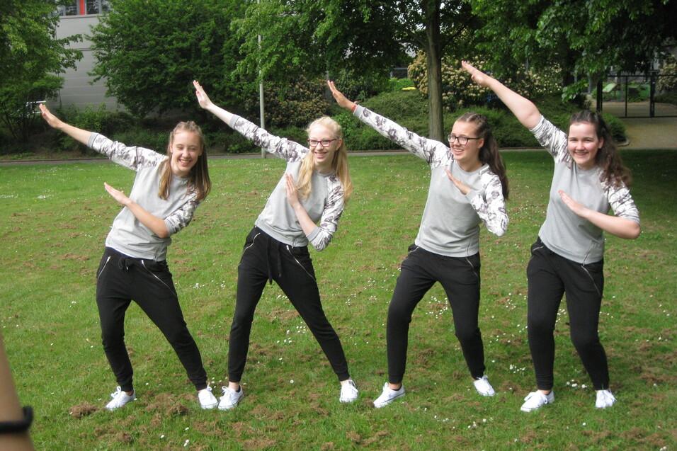 Vier junge Frauen in sportlicher Kleidung posieren gemeinsam im Freien auf einer Wiese.