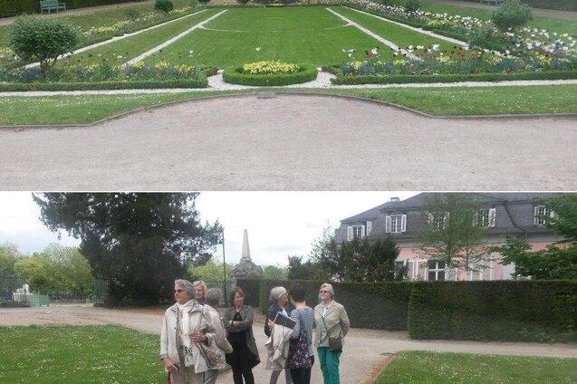 Gruppe von Menschen in einem Park mit Blumenbeeten und verwinkelten Wegen, im Hintergrund eine historische Geb&auml;udeansicht.