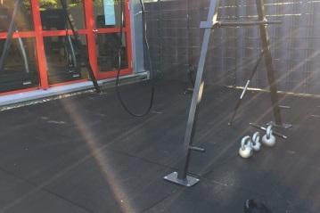 Fitnessbereich mit einem Trainingsger&auml;t, einer Klimmzugstange und zwei Kettlebells auf rutschfester Fl&auml;che.