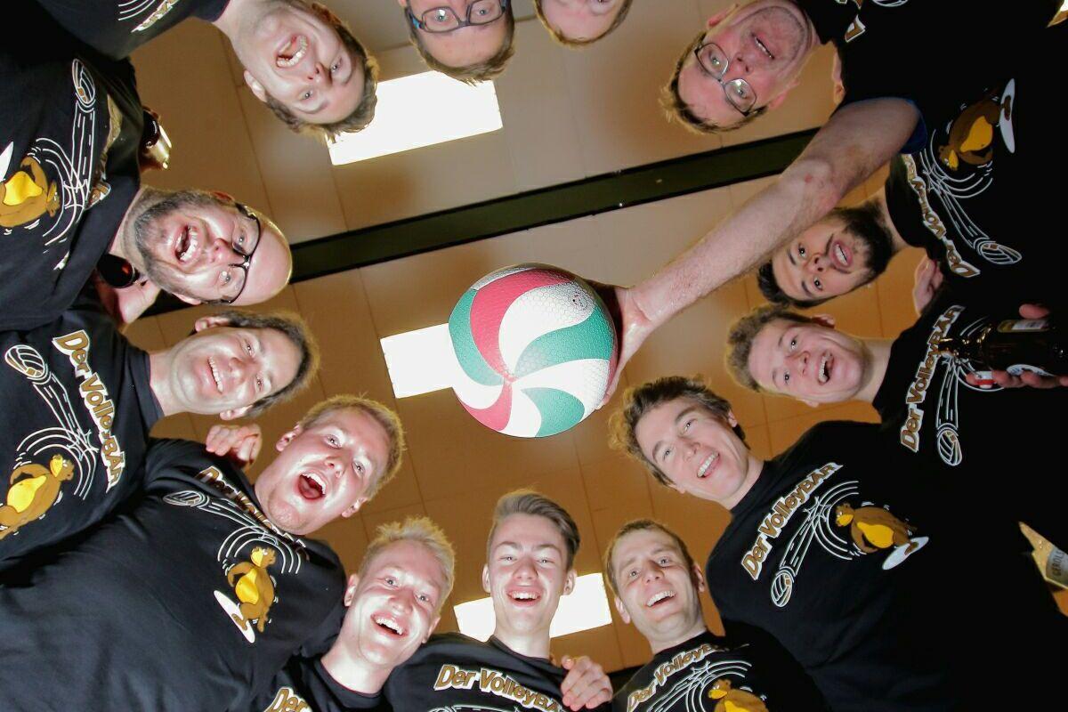 Gruppenselfie von zw&ouml;lf M&auml;nnern in schwarzen T-Shirts, die gemeinsam einen bunten Volleyball von oben halten.