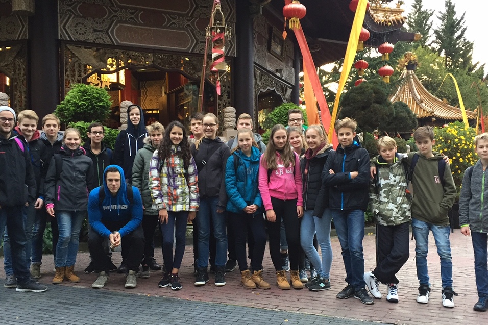 Gruppe von Jugendlichen posiert vor einem asiatischen Geb&auml;ude mit bunten Dekorationen und Pflanzen.