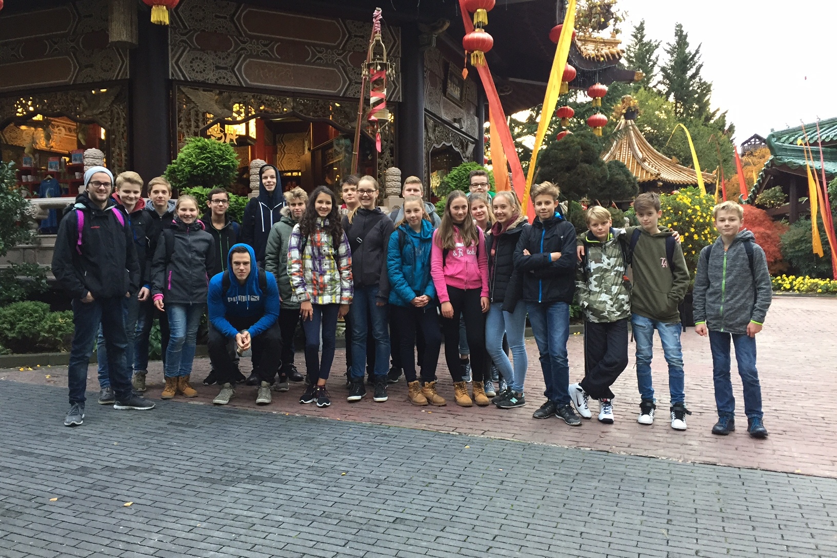 Gruppe von Jugendlichen posiert vor einem asiatischen Geb&auml;ude mit bunten Dekorationen und Pflanzen.