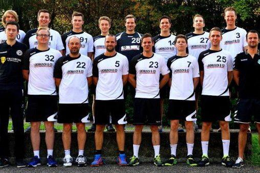 Mannschaftsfoto einer Handballmannschaft in einheitlichen Trikots, auf einer Wiese in der Natur aufgestellt.