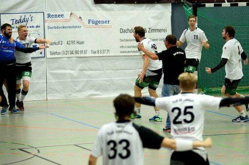 Handballspieler in weißen und schwarzen Trikots feiern einen Torwurf in einer Sporthalle.