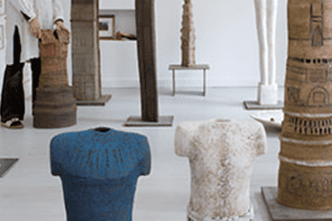 Skulpturen verschiedener Formen und Farben in einer Galerie, mit einer Person im Hintergrund.