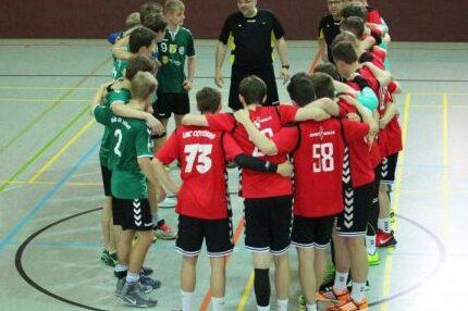 Zwei Handballmannschaften in einem Kreis, w&auml;hrend ein Trainer Anweisungen gibt. Spieler in roten und gr&uuml;nen Trikots.