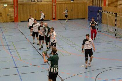 Spielszene in einer Handballhalle, Spieler in unterschiedlichen Trikots agieren w&auml;hrend eines Spiels auf dem Spielfeld.