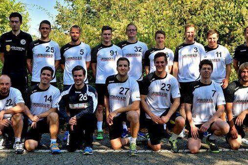 Gruppenfoto einer Fu&szlig;ballmannschaft mit 15 Spielern in Sportbekleidung auf einem Kiesplatz, umgeben von B&auml;umen.