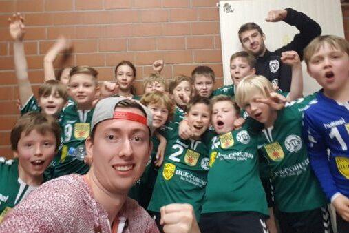 Gruppe junger Spieler in gr&uuml;nen Trikots posiert fr&ouml;hlich f&uuml;r ein Gruppenfoto in einem Umkleideraum.