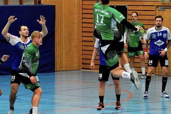 Aktion im Handballspiel: Spieler springt zum Wurf, w&auml;hrend Gegner in blauen Trikots versuchen, ihn zu blockieren.