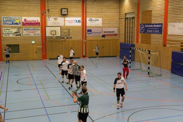 Spielszene in einer Handballhalle, Spieler in unterschiedlichen Trikots agieren w&auml;hrend eines Spiels auf dem Spielfeld.