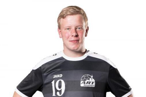 Ein junger Mann in einem schwarz-weißen Fußballtrikot mit der Nummer 19 steht mit verschränkten Armen vor einem weißen Hintergrund.