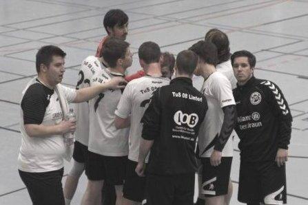 Gruppe von Handballspielern in wei&szlig;en und schwarzen Trikots, die sich in einer Halle besprechen.