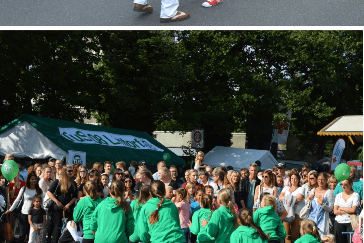Tanzende Menschen auf einem Handwerkermarkt, umgeben von Zuschauern und Veranstaltungsgel&auml;nden.