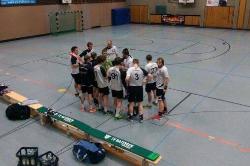Eine Gruppe von Spielern versammelt sich in einem Sportgymnasium zu einer Besprechung, B&auml;nke und Sporttaschen im Hintergrund.