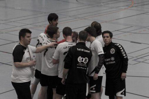 Eine Gruppe von Handballspielern versammelt sich in einer Halle f&uuml;r eine Besprechung, alle in einheitlichen Trikots.