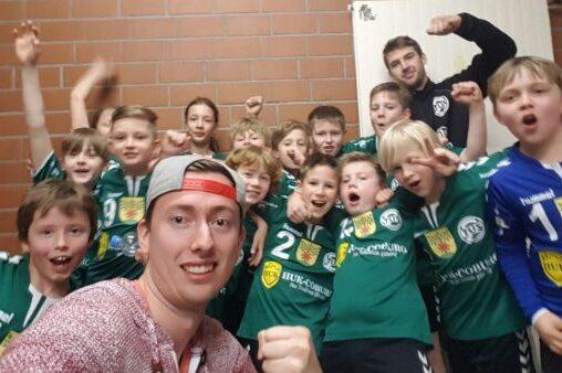 Gruppe junger Spieler in gr&uuml;nen Trikots posiert fr&ouml;hlich f&uuml;r ein Gruppenfoto in einem Umkleideraum.