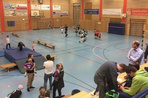 Sporthalle mit Kindern, die spielen und trainieren, umgeben von Erwachsenen, die zuschauen und sich unterhalten.