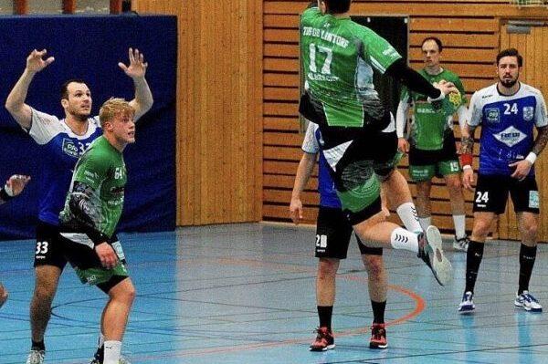 Aktion im Handballspiel: Spieler springt zum Wurf, w&auml;hrend Gegner in blauen Trikots versuchen, ihn zu blockieren.