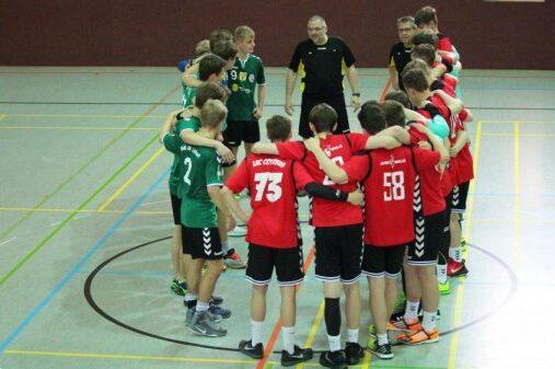Zwei Handballmannschaften in einem Kreis, w&auml;hrend ein Trainer Anweisungen gibt. Spieler in roten und gr&uuml;nen Trikots.