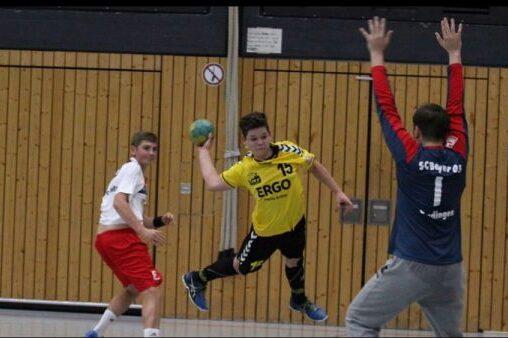 Handballspieler in gelb wirft auf das Tor, w&auml;hrend zwei Gegner in wei&szlig; und rot defending. Sporthalle mit Holzpaneelen im Hintergrund.