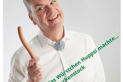 Mann in wei&szlig;em Hemd h&auml;lt eine Bratwurst und l&auml;chelt, vor hinterschnittenem Text zum Veranstaltungshinweis.