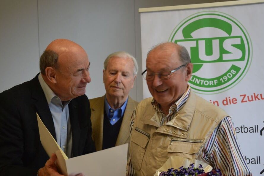 Drei M&auml;nner stehen bei einer Ehrung zusammen, einer h&auml;lt eine Urkunde, w&auml;hrend der andere Blumen erh&auml;lt.